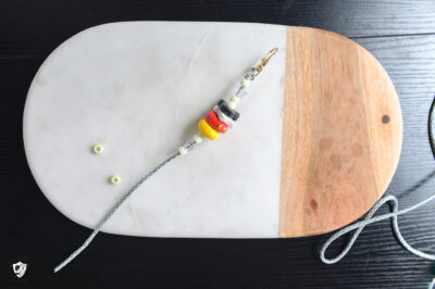 gray paracord on a lobster clasp on a marble slab, with white and clear plastic bead s and a stack of black, white, red, and yellow clay beads.