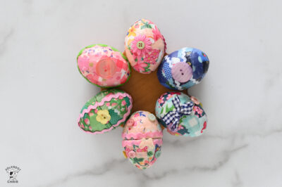tray with 3 pink eggs one green egg and 2 blue eggs all covered in ribbon, ricrac, and buttons.