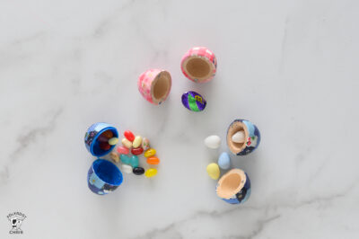 three eggs open with candy coming out of them the eggs are pink, blue, and teal.