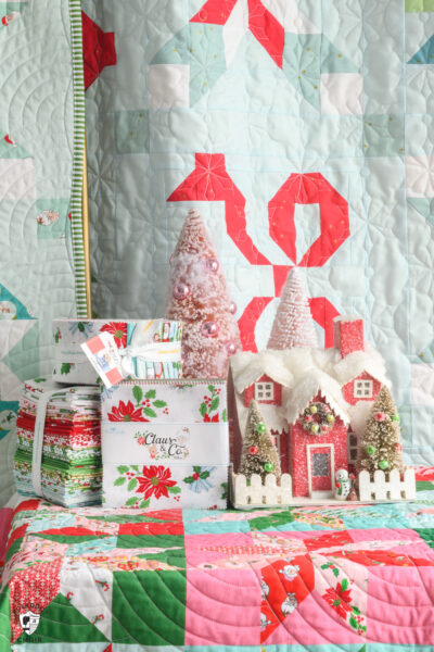 Christmas fabric and house in front of quilts on top of quilt table