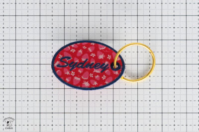Red oval keychain with blue 'Sydney' text and floral pattern.