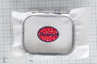 Close-up of a white fabric with a red and blue embroidered patch reading 'Sydney'.